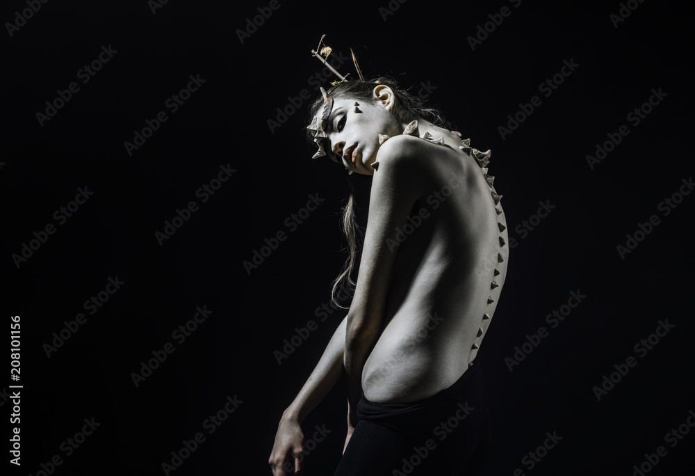 Brunette girl with thorns on face and spikes on bare back isolated on black background. Forest nymph with horns and messy hair, wilderness and fantasy concept Brunette girl with thorns on face and spikes on bare back isolated on black background. Forest nymph with horns and messy hair, wilderness and fantasy concept
