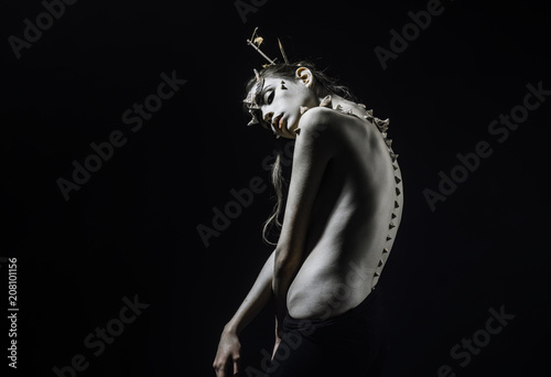 Brunette girl with thorns on face and spikes on bare back isolated on black background. Forest nymph with horns and messy hair, wilderness and fantasy concept