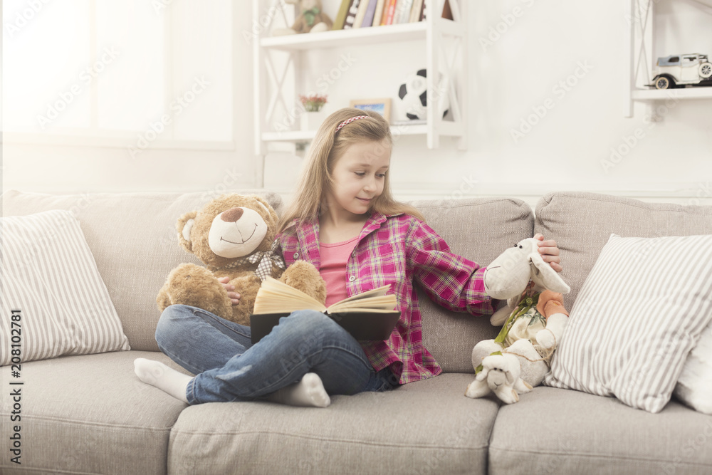 Happy little child reading book for her teddy bear Happy little child reading book for her teddy bear