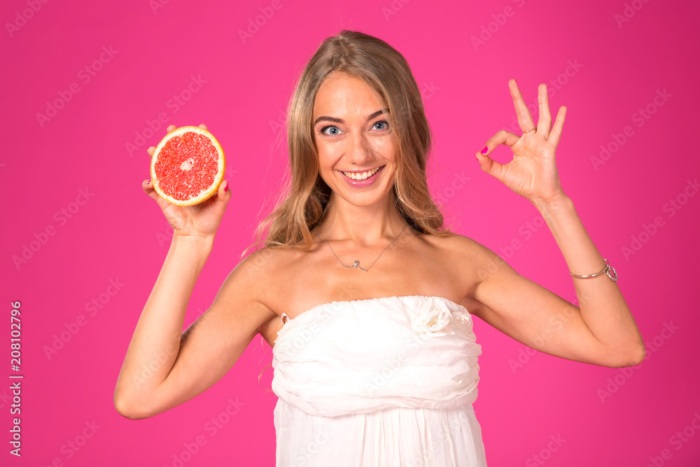 Ok! Beautiful blonde woman with a grapefruit in hands on a pink background. Showing OK sign. Ok! Beautiful blonde woman with a grapefruit in hands on a pink background. Showing OK sign.