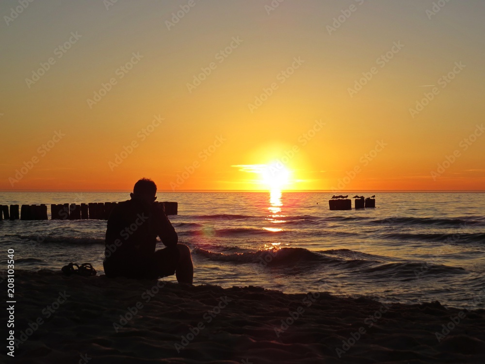 Man Sitting on Sand Beach Seaside during Sunset with Clouds