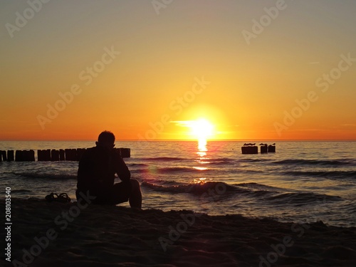 Man Sitting on Sand Beach Seaside during Sunset with Clouds