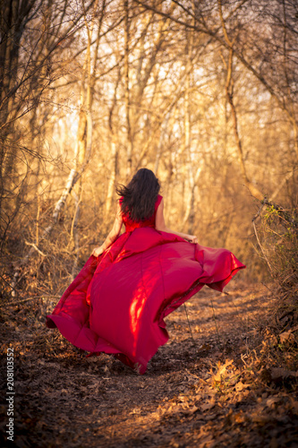 Girl in red dress running through woods