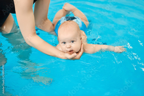 Little baby swimming in water pool with help from mothers hands. © Suslov Denis