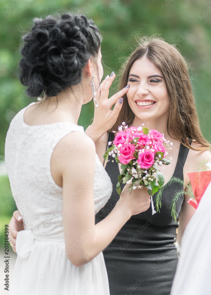 Portrait of two young beautiful women friends. Pretty bride with roses bouquet helping her smiling bridesmaid. Wedding at Sunny summer day in green park Portrait of two young beautiful women friends. Pretty bride with roses bouquet helping her smiling bridesmaid. Wedding at Sunny summer day in green park