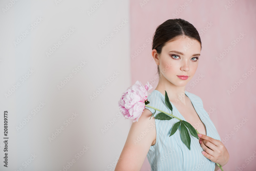 A young woman with gathered hair is standing holding a peony in her hands. A young woman with gathered hair is standing holding a peony in her hands.
