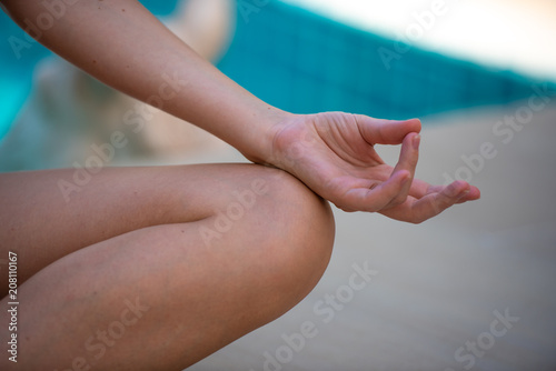 Young healthy woman with blonde curly hair doing yoga meditation at swimming pool, weekend vacation and relaxing concept.