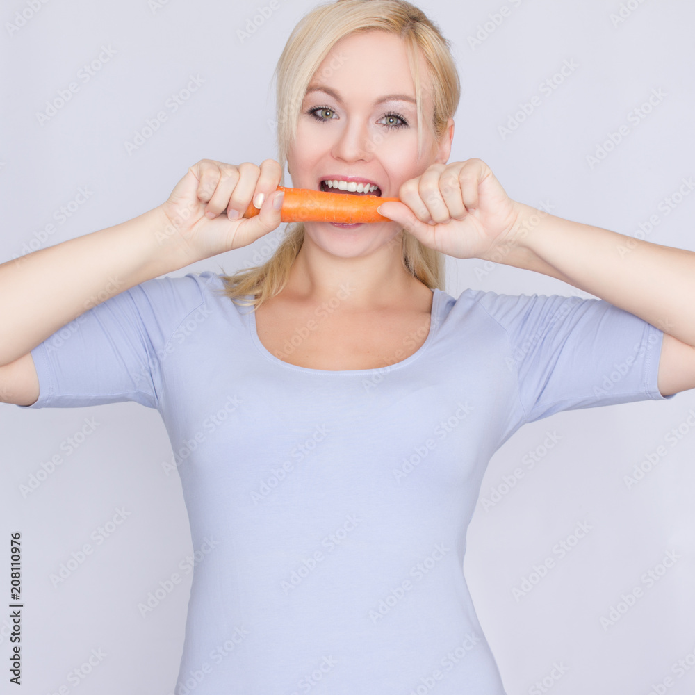 Young blond woman biting young large carrots with her teeth Young blond woman biting young large carrots with her teeth
