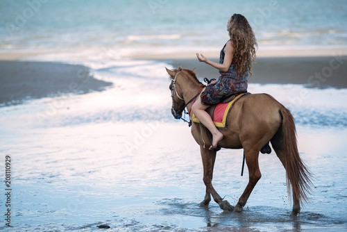 Happy smiling attractive blond curly hair woman riding a horse on the Beach, relaxing time concept. © May_Chanikran