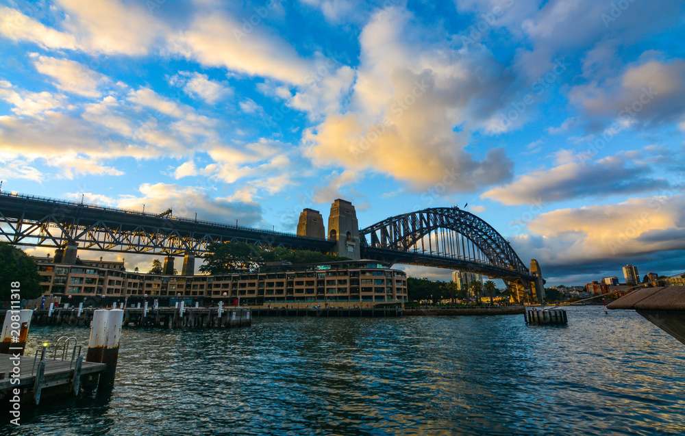 Naklejka premium Sunset and evening clouds over Sydney Harbour Bridge as seen from the docks at Circular Quay