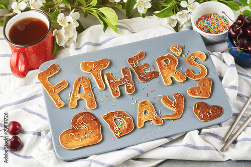 Special Father's Day breakfast. Alphabet Pancakes with sprinkles, cherries and cup of tea on a gray concrete background