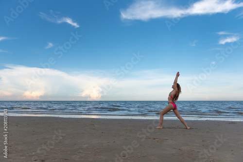 Young healthy woman with blonde curly hair practicing yoga on the beach, Summer beach vacation and relaxing concept.