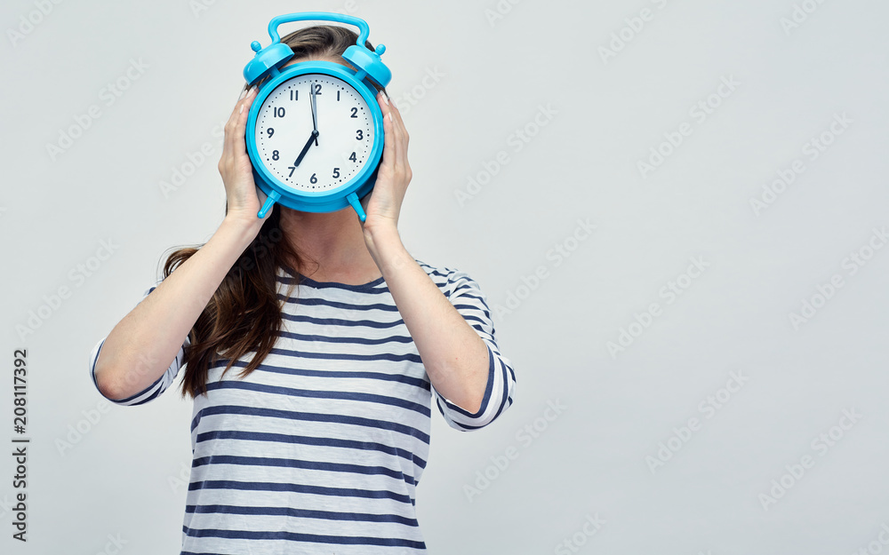Woman wearing striped shirt holding alarm clock in front of face Woman wearing striped shirt holding alarm clock in front of face