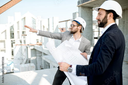 Two business men or engeneers working with house drawings on the structure during the construction process outdoors photo