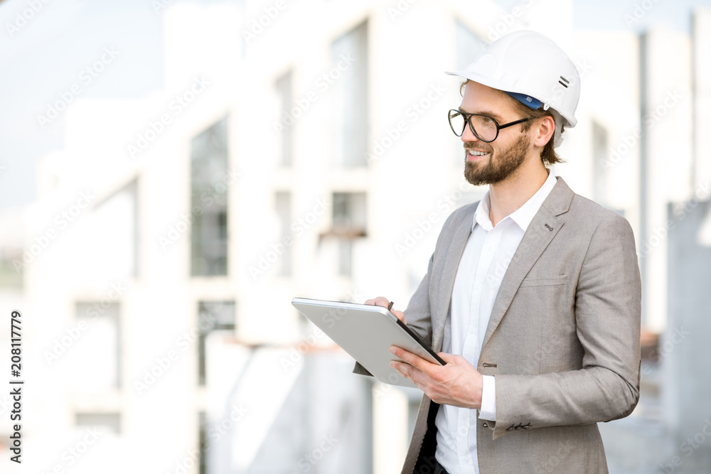 Handsome engineer working with tablet standing on the structure site with a new house on the background