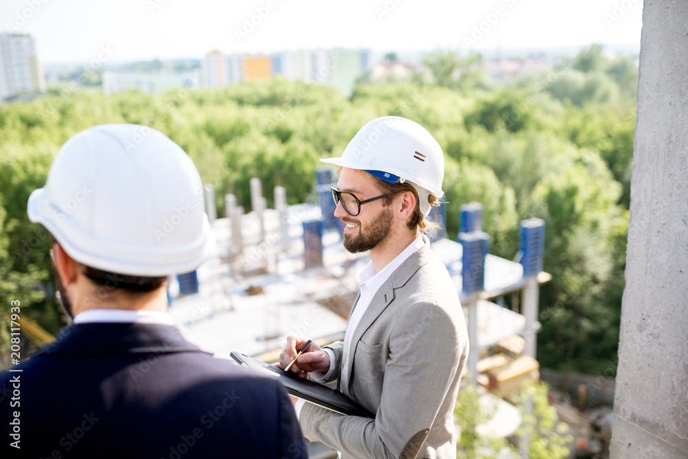 Two engineers or architects supervising the process of residential building construction standing on the structure outdoors Two engineers or architects supervising the process of residential building construction standing on the structure outdoors