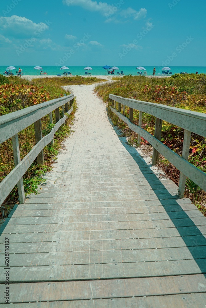 Dramatic vertical view of Wood Bridge looking toward a sandy Sanibel Beach on Sanibel Island with colorful umbrellas on a sunny day before Hurricane Ian