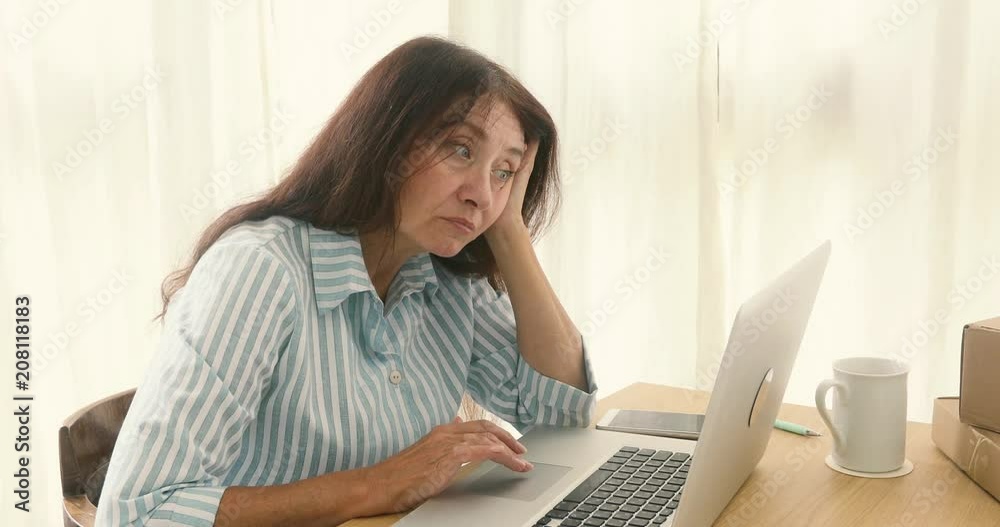 Mature woman bored sitting while flipping the internet laptop in home office Mature woman bored sitting while flipping the internet laptop in home office