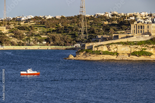 A red and white motorboat passes along the Kalkara coastline, Rinella Bay Kalkara Malta, part of the Bighi Complex photo