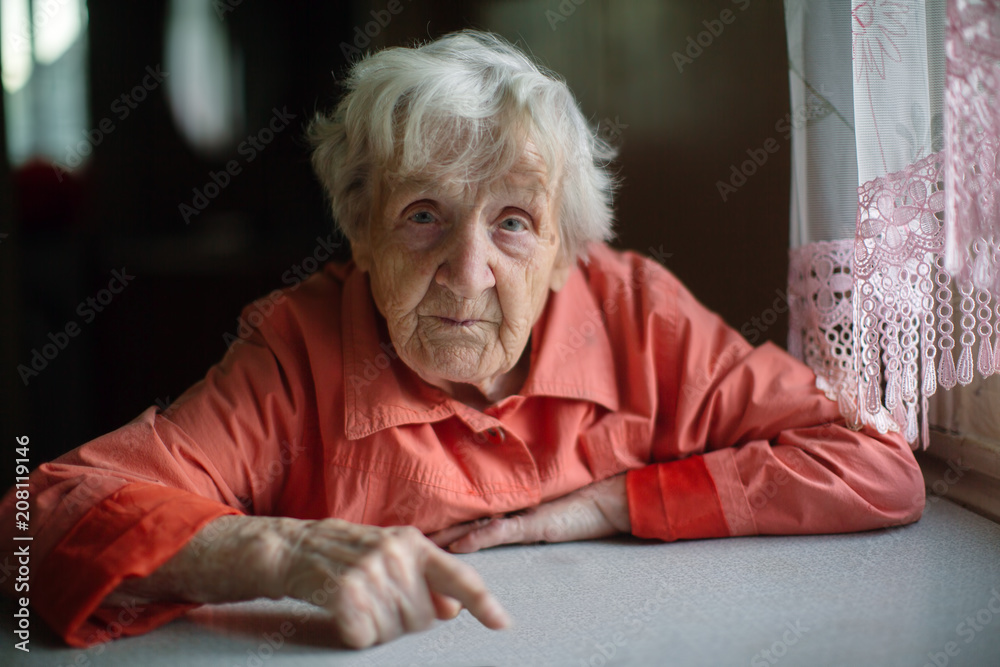 An elderly lady sitting near the window in the kitchen. An elderly lady sitting near the window in the kitchen.