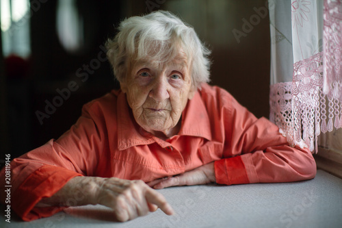 An elderly lady sitting near the window in the kitchen.