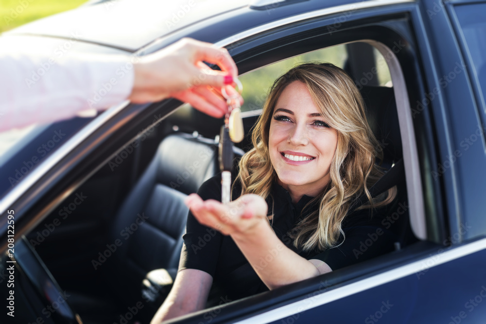 An attractive woman in a car gets the car keys. Rent or purchase of auto. - obrazy, fototapety, plakaty 