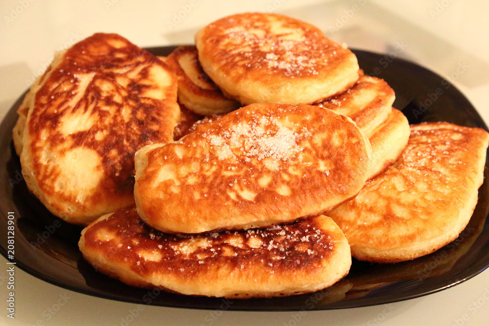 Pancakes sprinkled with sugar on a black plate. Pancakes with milk. Close-up.
