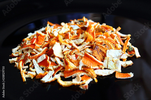 Finely chopped dried mandarin peel on a black plate. Isolated. Close-up.