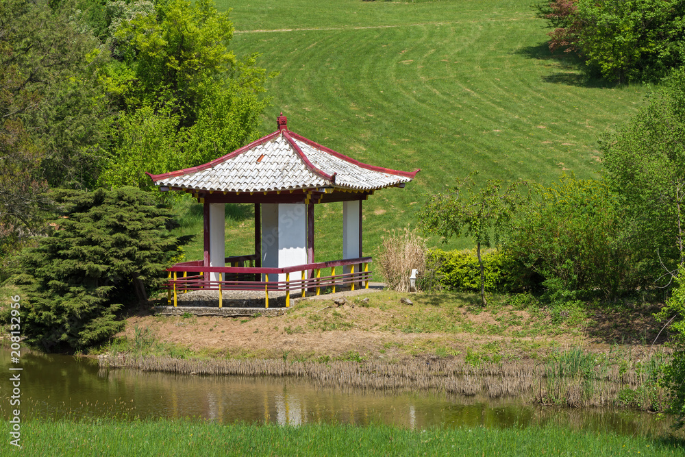 gazebo with white roof stands on the shore of the lake