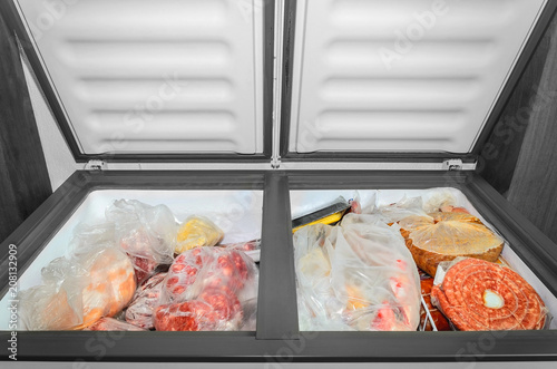 Frozen food in the freezer. Bagged frozen meat and other foods in a horizontal freezer with the two doors open. Food preservation. photo
