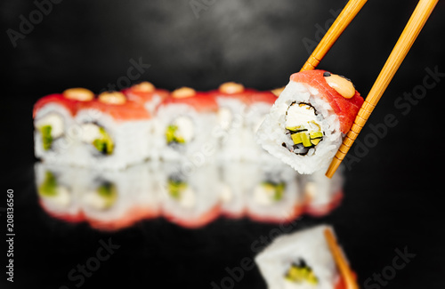 Chopsticks holding Sushi Roll Philadelphia with fresh tuna with smoked salmonon black background made of Seaweed, marinated rice, cheese Philadelphia, Sushi menu. Japanese food. Free-space. Close-up. photo