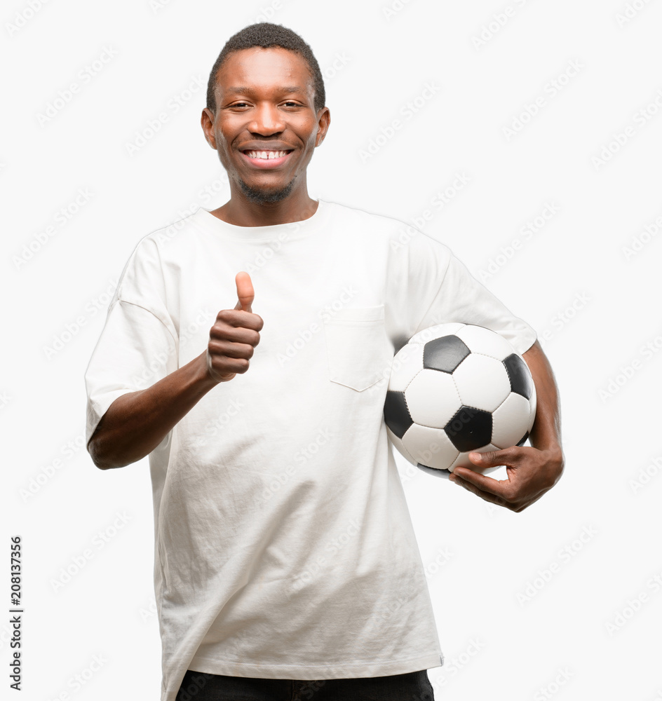 African black man holding soccer ball smiling broadly showing thumbs up gesture to camera, expression of like and approval African black man holding soccer ball smiling broadly showing thumbs up gesture to camera, expression of like and approval