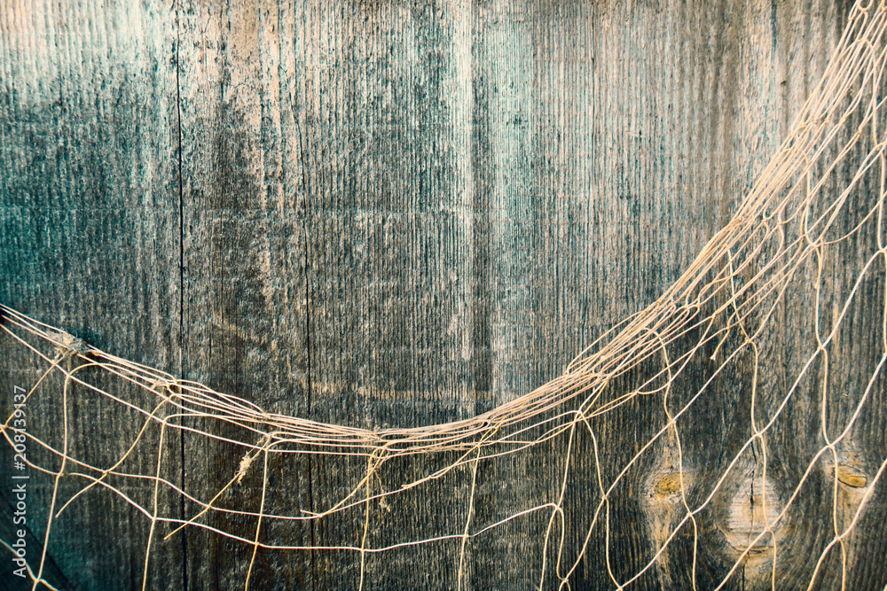 Fishing nets over wooden background with copy space. Fishing nets on wooden  background. Hanging Fishnet on Wood Wall. Fishing net on vintage wood,  maritime nautical background texture. Stock Photo