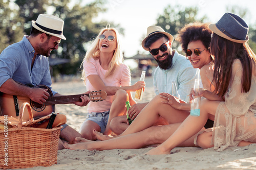 Group of friends with guitar having fun on the beach