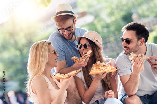 Close up of four young cheerful people eating pizza.