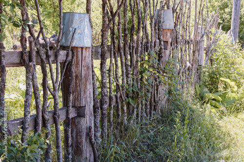 Rural fence made of old logs and branches decorated with old tin buckets