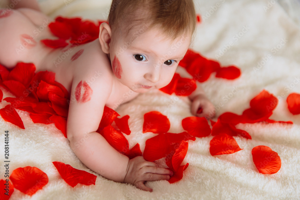 A brown-eyed little girl in kisses from a lipstick lies on the bed. Child in red rose petals. A brown-eyed little girl in kisses from a lipstick lies on the bed. Child in red rose petals.