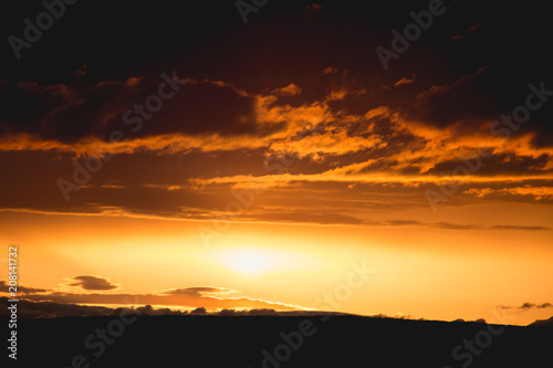 orange clouds and golden sun beam at sunset horizon