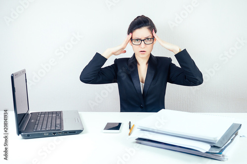 attractive smart brunette woman (business lady) in stylish business suit and glasses working with laptop and screams in panic in office . business concept and deadline