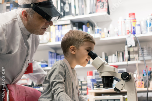 Little boy looking through microscope with help of his teacher.