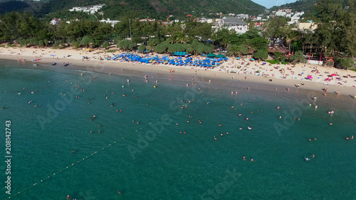 Man flies on parachute above sea near Kata beach Phuket with many tourists get rest on beach at summer sunny day