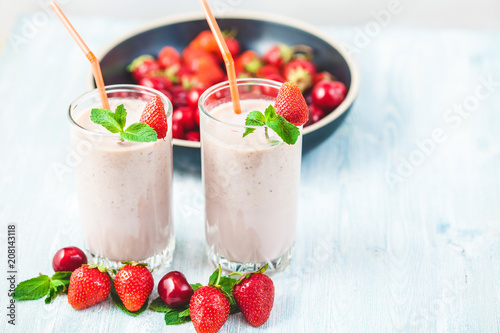 two glasses of smoothies made from milk, strawberries, banana, cherries, decorated with mint on bright white background Concept healthy lifestyle, diet, tasty Copy space