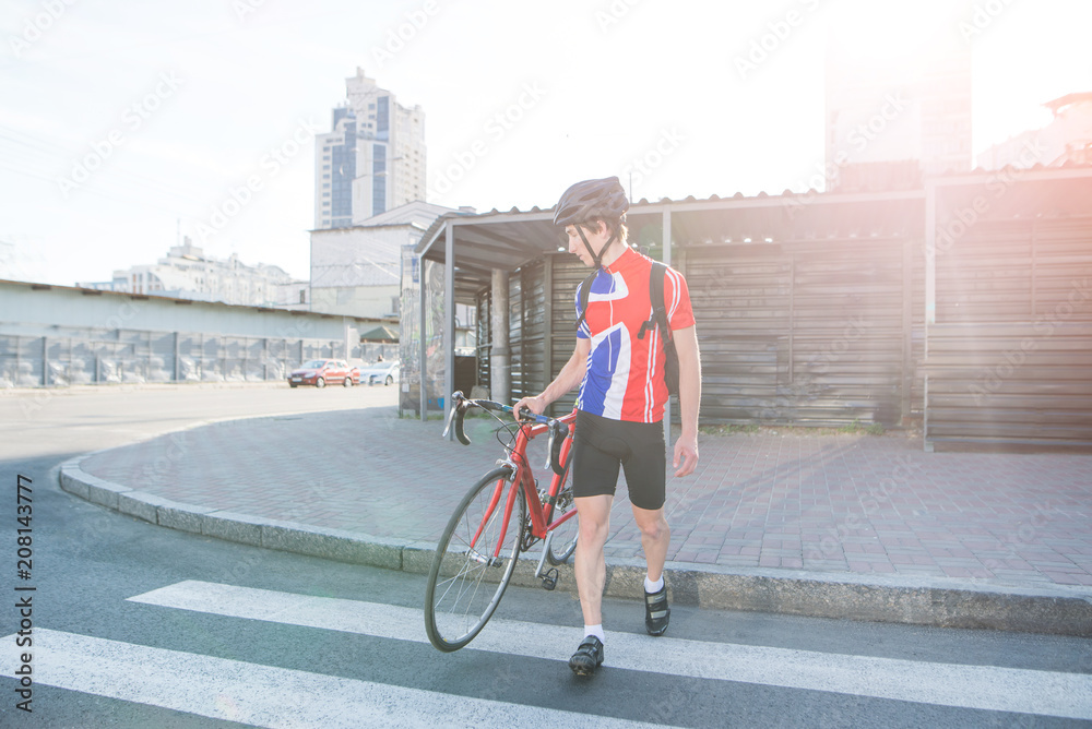 Professional cyclist in sportswear and a helmet crosses the zebra road against the backdrop of sunlight. A man goes on a zebra hike with a bike in his hands. Traveling around the city on a bicycle.
