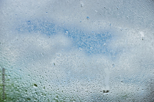 drops of summer rain on the window glass of fresh blue and white clouds background texture
