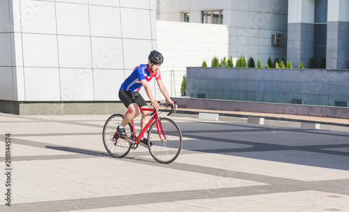 Young man in Cycle Clothing rides a road bike on a background of modern architecture. Sports concept. Cyclist cycles around the city.