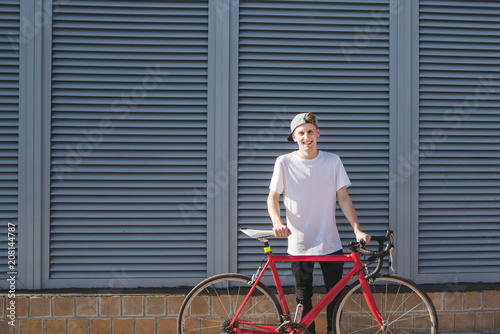 Portrait of a smiling handsome man on a bicycle on a background of gray walls. Hipster with a red bike stands against the wall and smiles
