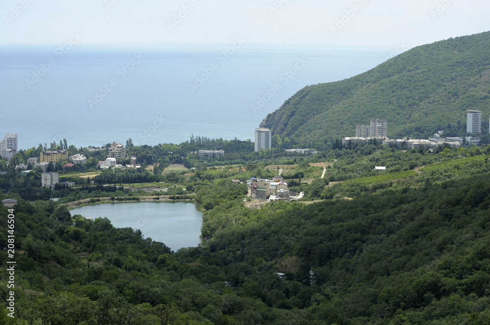 View of a small resort town Krasnokamenka and a lake situated at a foothill of a mountain, sea in the background. June 11, 2017. Crimea