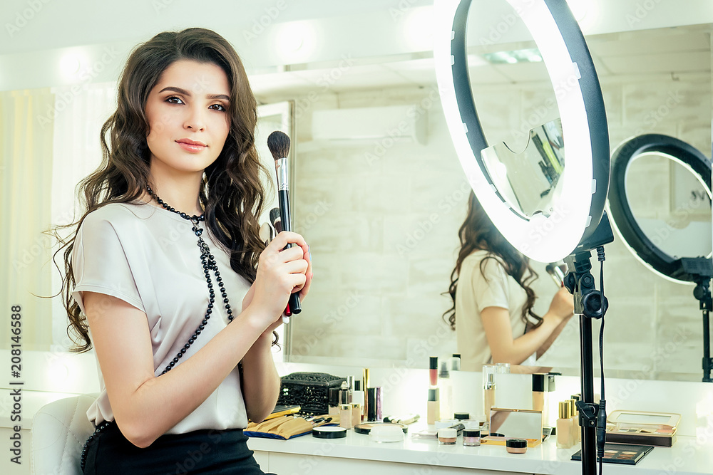 charming beautiful woman make-up artist (visagiste ) sitting in front of a  mirror and holding a brushes cosmetics make-up on face in studio Stock  Photo | Adobe Stock