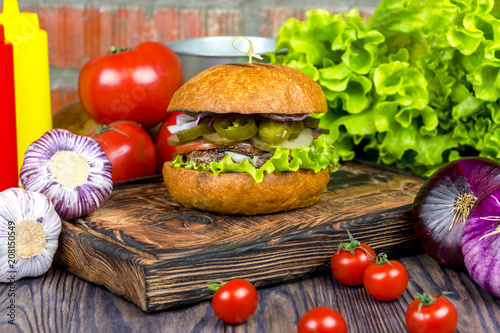 Appetizing burger on a wooden board against a background of vegetables