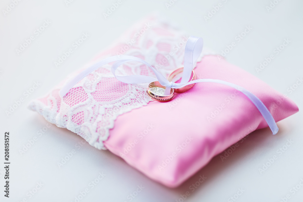 Wedding rings with diamonds lie waiting for the wedding moment, on the pink ceremonial small pillow covered with thin lace.